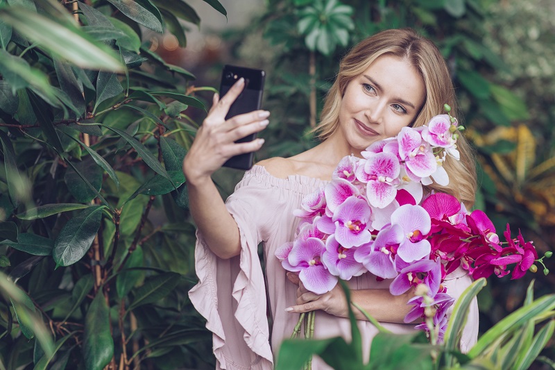 smiling-young-woman-holding-beautiful-orchid-branches-in-hand-taking-selfie-on-smart-phone.jpg