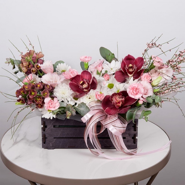 Pink Cymbidium Orchid Bud - 3, Pink Lisianthus (Eustoma) - 3, Pink spray carnation - 5, White Delphinium - 2, Bacardi White Spray Chrysanthemum - 1, Baltica White Spray Chrysanthemum - 1, Wooden pot, Oasis, Wrapping Paper, Flask for orchids, Eucalyptus, Genista